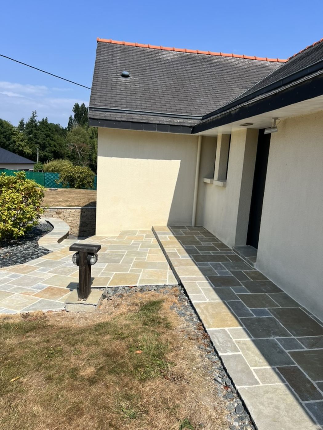 Aménagement extérieur par Nouvel Espace — terrasse en pierre naturelle le long de la maison